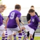 Image of a group of kids wearing team sport shirts while playing soccer.