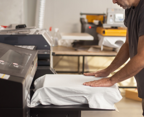 Side view of a man using machine to print graphic on tshirt